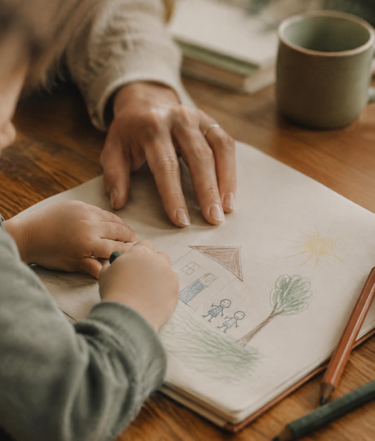 A parent's hand next to a child drawing in a notebook